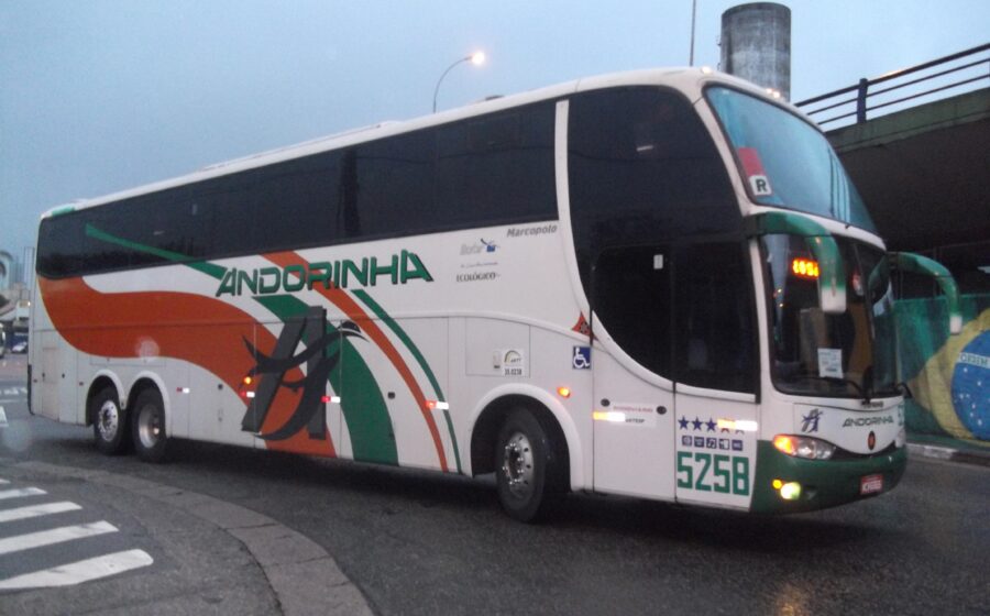 Ônibus interestaduais parados em terminal com prédio da ANTT ao fundo simbolizando burocracia travada