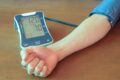 Smartphone exibindo app Elfie ao lado de monitor de pressão arterial mostrando redução de 4,8 mmHg