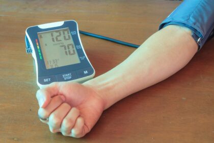 Smartphone exibindo app Elfie ao lado de monitor de pressão arterial mostrando redução de 4,8 mmHg
