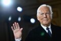 Giorgio Armani em escritório com logotipo da marca, simbolizando negociação de venda bilionária