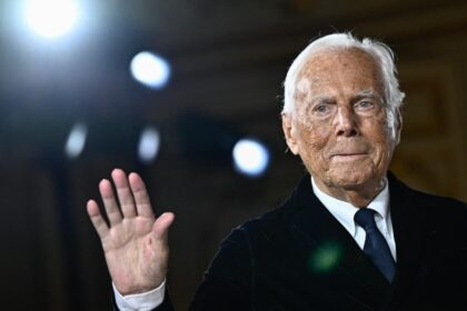 Giorgio Armani em escritório com logotipo da marca, simbolizando negociação de venda bilionária