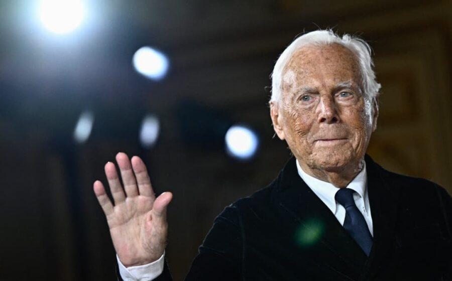 Giorgio Armani em escritório com logotipo da marca, simbolizando negociação de venda bilionária