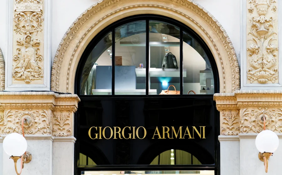 Retrato de Giorgio Armani com logotipos LVMH e L'Oréal, simbolizando negociação de venda de 15% do grupo