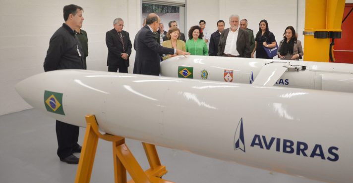 Foguete Avibras ASTROS 2020 em plataforma de lançamento com bandeira do Brasil ao fundo