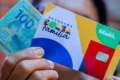Cartão do Bolsa Família com nota de 100 reais sobre mesa, simbolizando reajuste de 15% no benefício social