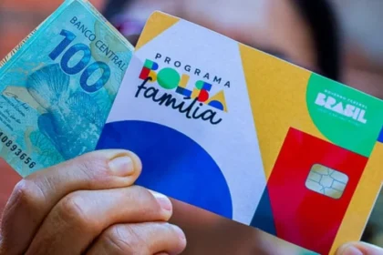 Cartão do Bolsa Família com nota de 100 reais sobre mesa, simbolizando reajuste de 15% no benefício social