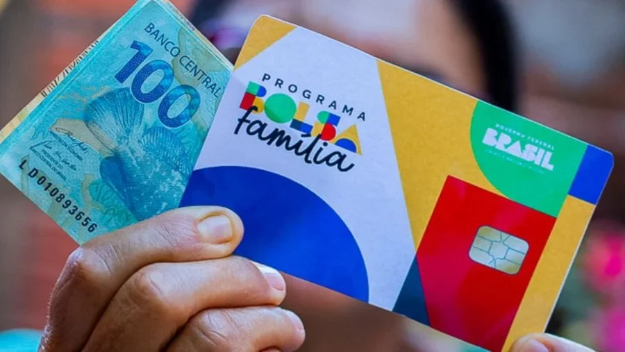 Cartão do Bolsa Família com nota de 100 reais sobre mesa, simbolizando reajuste de 15% no benefício social