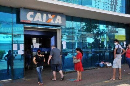Agência da Caixa Econômica Federal com portas parcialmente abertas durante greve, clientes na fila e aviso de atendimento reduzido