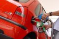 Bomba de gasolina com preço alto e carro novo em concessionária representando custo oculto de regra de Trump