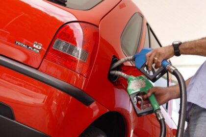 Bomba de gasolina com preço alto e carro novo em concessionária representando custo oculto de regra de Trump