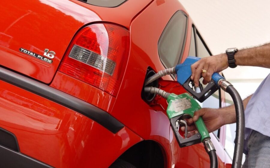 Bomba de gasolina com preço alto e carro novo em concessionária representando custo oculto de regra de Trump