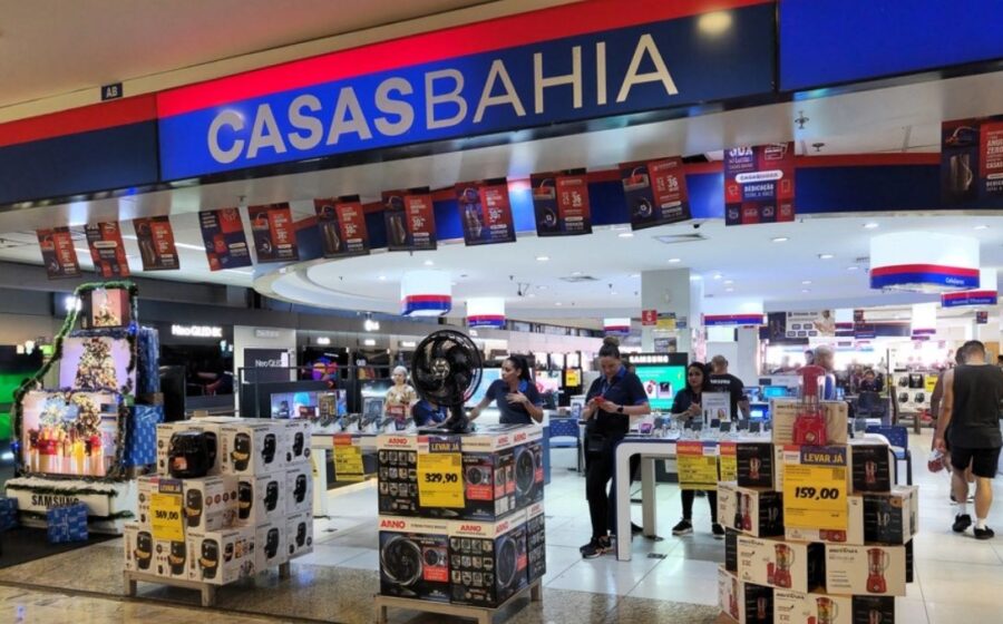 Fachada da loja Casas Bahia com logotipo da empresa e martelo de juiz sobre documentos jurídicos