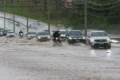 Rua alagada no Distrito Federal com carros parcialmente submersos e água barrenta cobrindo asfalto