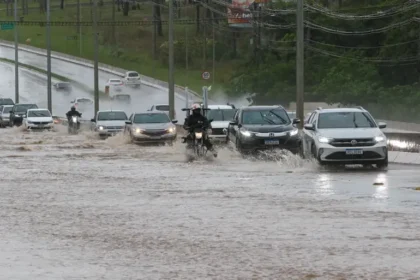 Rua alagada no Distrito Federal com carros parcialmente submersos e água barrenta cobrindo asfalto