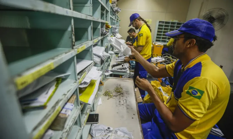 Carteiro dos Correios em frente a agência durante greve com faixa de paralisação