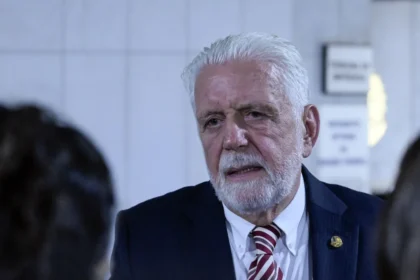 Senador Jaques Wagner em sessão no Congresso, com sobreposição de notas de R$ 100 e documentos de investigação