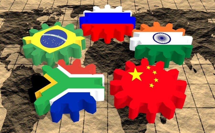 Tabuleiro geopolítico com IA, satélites e bandeiras dos BRICS representando disputa tecnológica 2026