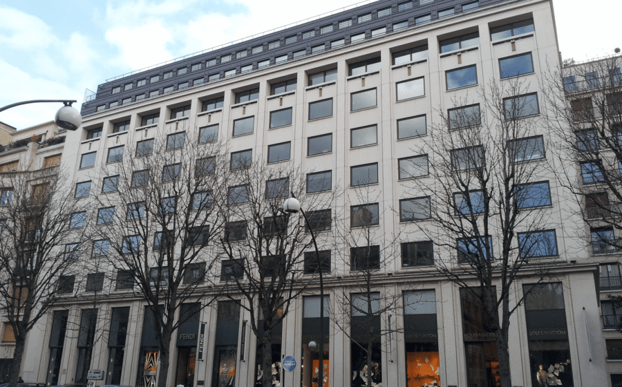 Sede da LVMH em Paris com logotipo Louis Vuitton e gráfico de queda acionária