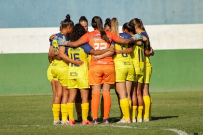 Jogadoras de futebol feminino comemorando gol em estádio brasileiro, representando nova lei de investimento obrigatório