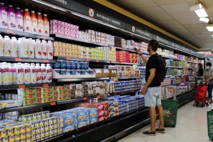 Carrinho de supermercado com produtos básicos e etiquetas de preço alto, simbolizando inflação alimentar pré-eleição