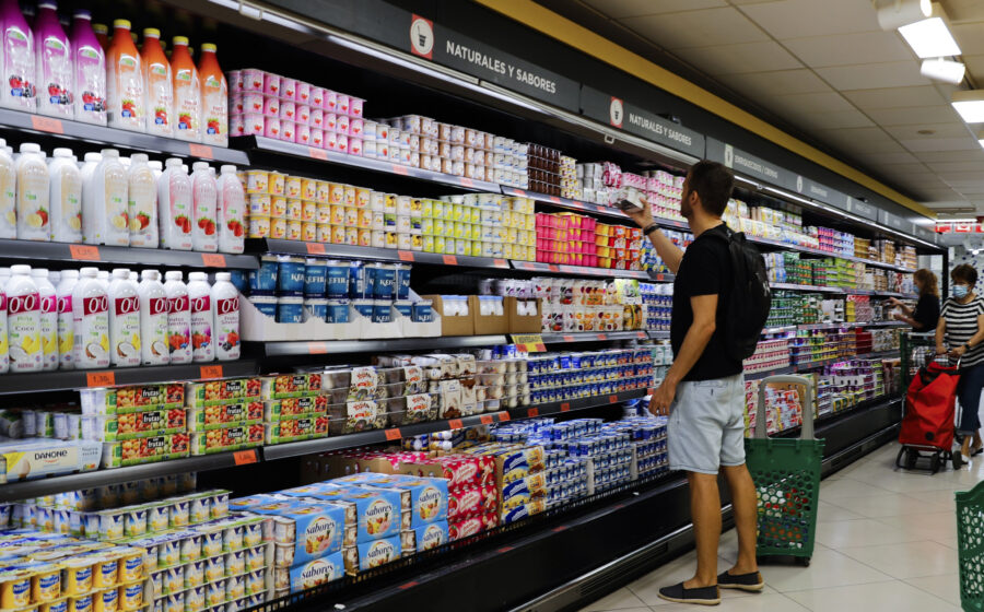Carrinho de supermercado com produtos básicos e etiquetas de preço alto, simbolizando inflação alimentar pré-eleição