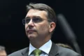 Flávio Bolsonaro em destaque com símbolos de risco político e carta democrática ausente