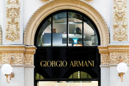 Giorgio Armani em fundo preto com logos da LVMH, L'Oréal e EssilorLuxottica representando negociação de 15% do grupo