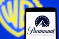 Logos da Paramount e Warner Bros. Discovery sobre fundo financeiro simbolizando fusão de US$ 80 bi