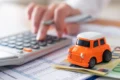 Carro zero-quilômetro em concessionária brasileira com calculadora e documentos de impostos sobre o capô