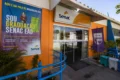 Fachada do Senac Rio das Ostras com alunos e ícones de cursos gastronomia e IA