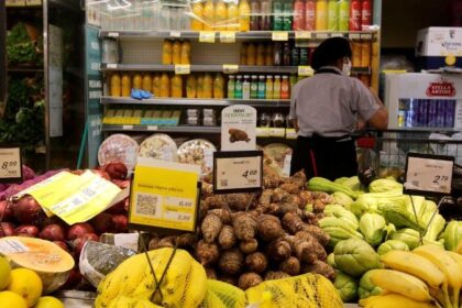 Supermercado aberto em feriado com clientes fazendo compras, faixa indicando funcionamento normal