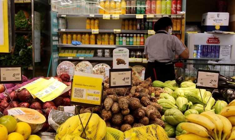 Supermercado aberto em feriado com clientes fazendo compras, faixa indicando funcionamento normal