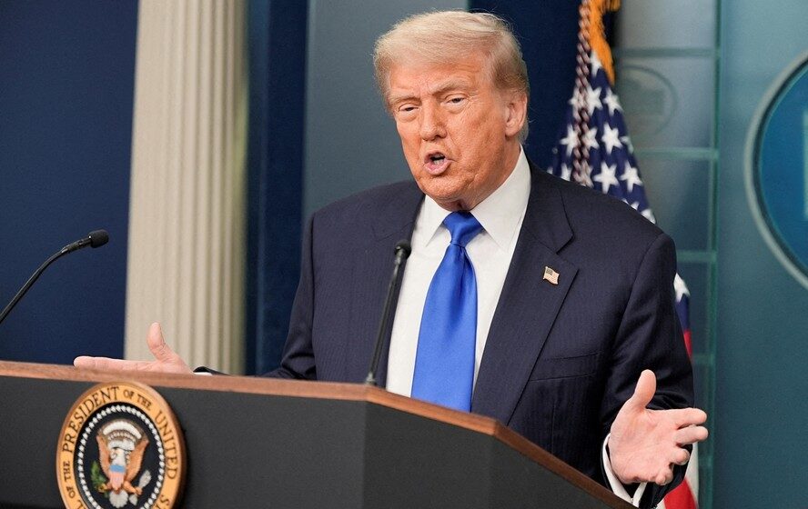 Trump em posto de gasolina ao lado de carro, simbolizando flexibilização de metas de eficiência veicular nos EUA