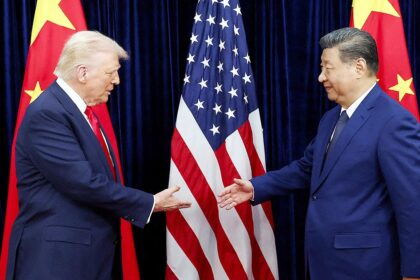Trump e Xi Jinping apertam as mãos em cúpula diplomática com bandeiras dos EUA e China ao fundo