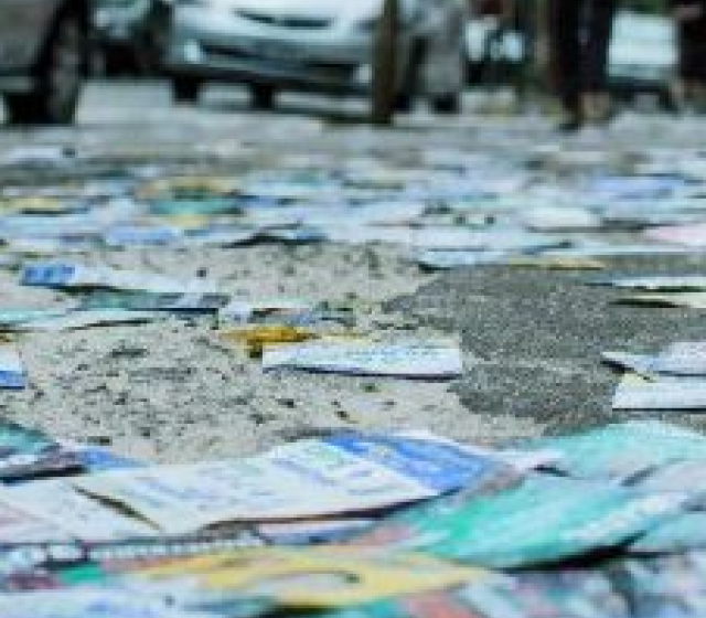 Santinhos eleitorais espalhados no chão de rua urbana, simbolizando crime eleitoral e risco ambiental