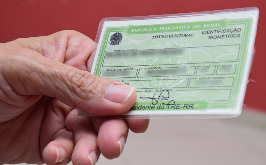 Smartphone exibindo o aplicativo e-Título aberto na tela inicial com fundo de urna eletrônica