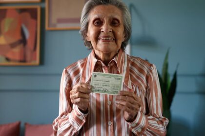 Idosa votando em urna eletrônica com campanha Vovó Vota ao fundo