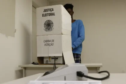 Eleitor na seção eleitoral com urna eletrônica e aviso "Proibida boca de urna" em destaque