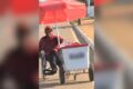 Cadeirante empurra carrinho de picolés com uma mão enquanto impulsiona cadeira de rodas na avenida de Palmas