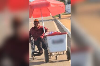 Cadeirante empurra carrinho de picolés com uma mão enquanto impulsiona cadeira de rodas na avenida de Palmas