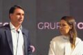 Flávio Bolsonaro discursa com logotipo da Caixa Econômica Federal e imagem de comunidade periférica ao fundo