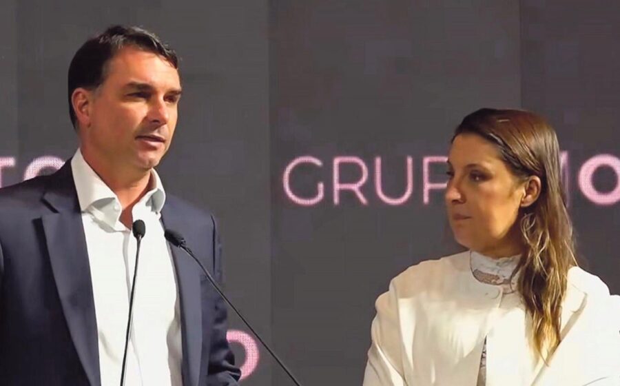 Flávio Bolsonaro discursa com logotipo da Caixa Econômica Federal e imagem de comunidade periférica ao fundo