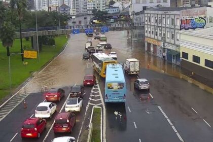 Motociclistas em motociata sob chuva forte na avenida de Porto Alegre, com bandeiras do Brasil