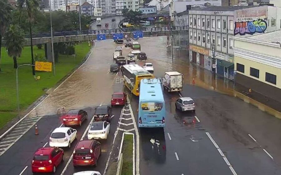 Motociclistas em motociata sob chuva forte na avenida de Porto Alegre, com bandeiras do Brasil
