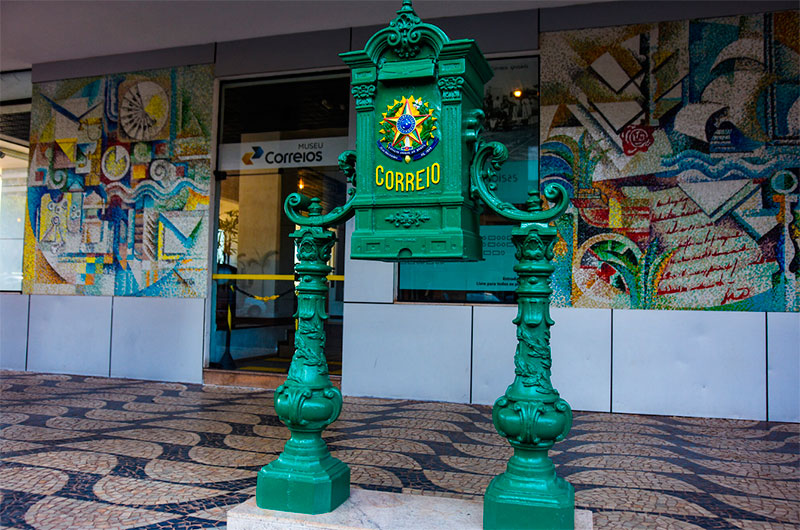 Edifício dos Correios em Brasília com logotipo da estatal e símbolos de recursos financeiros