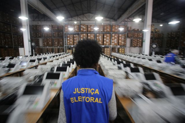 Eleitor olha apreensivo para celular exibindo vídeo deepfake de candidato com alerta vermelho "MANIPULADO"