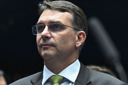 Flávio Bolsonaro em coletiva contestando resultado eleitoral com logo do PL ao fundo