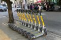 Patinetes elétricos compartilhados estacionados em calçada de São Paulo com skyline urbano ao fundo