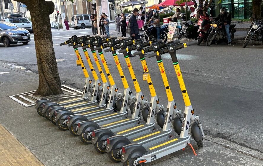 Patinetes elétricos compartilhados estacionados em calçada de São Paulo com skyline urbano ao fundo