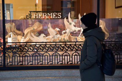 Bolsas Hermès Birkin e Kelly sobre gráfico de ações em queda, simbolizando recuo de 6% apesar de lucro crescente